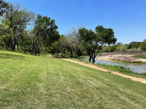 A serene landscape featuring a grassy area, trees, and a calm river under a clear blue sky.