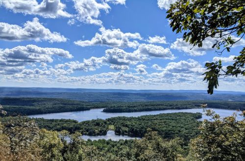 A scenic view of a river winding through lush green forests under a bright blue sky with fluffy white clouds.