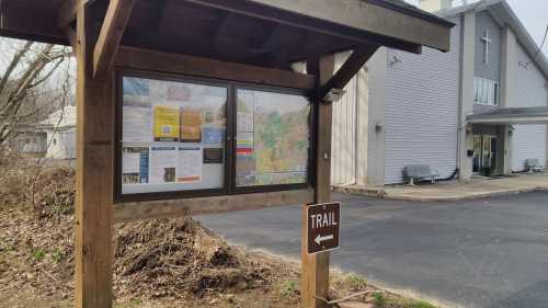 A wooden trail sign with a map and information board next to a building, indicating the start of a trail.