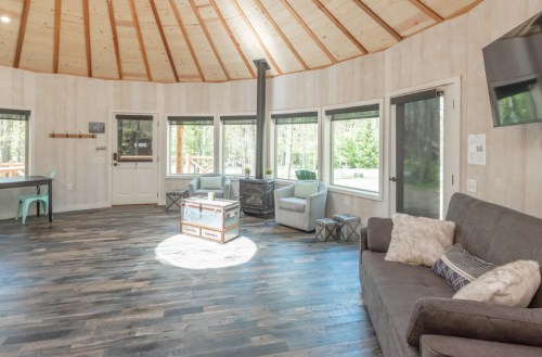 A spacious, circular living area with wooden walls, large windows, and cozy seating around a central light.