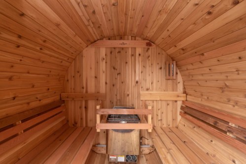 Interior of a wooden sauna with cedar walls, a stove in the center, and benches along the sides.