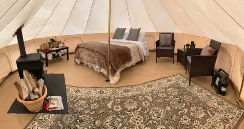 Cozy glamping tent interior with a bed, seating area, wood stove, and decorative rug.