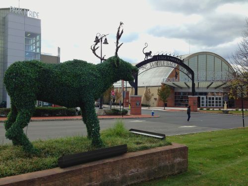 A large topiary moose stands in front of a building with an archway sign and cloudy skies above.