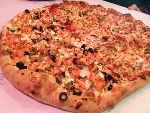 A large pizza with a variety of toppings, including olives, green peppers, and cheese, on a golden crust.