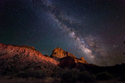 A stunning night sky filled with stars and the Milky Way over rugged mountain peaks and desert landscape.