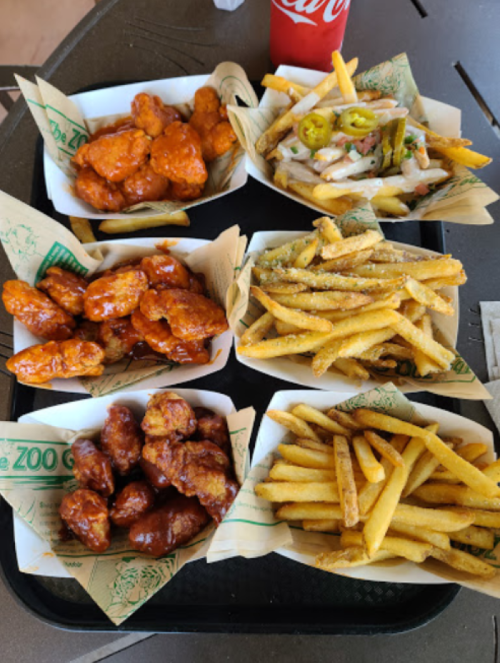 A tray of various food items: chicken wings in sauce, loaded fries, and regular fries, with a soda in the background.