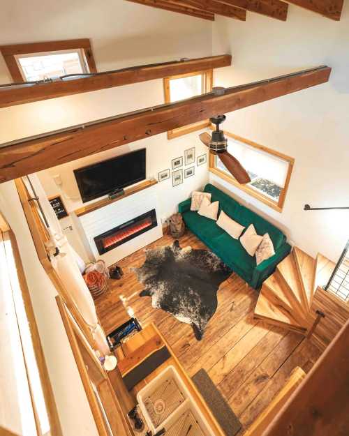 A cozy living room with a green sofa, wooden beams, a fireplace, and a spiral staircase, featuring rustic decor.