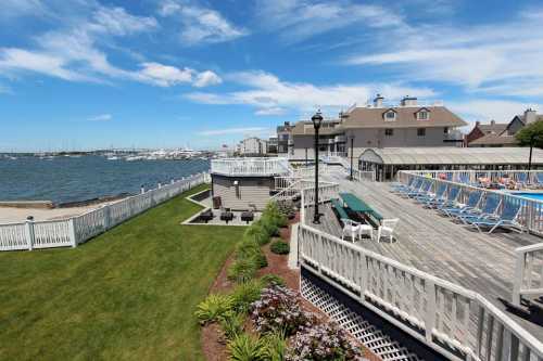 A scenic view of a waterfront property with a grassy area, deck, and boats in the distance under a blue sky.