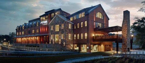 A modern building with a mix of stone and brick, featuring large windows and a deck, set against a cloudy sky.