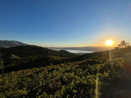 A scenic view of rolling hills and a lake at sunset, with vibrant greenery and mountains in the background.