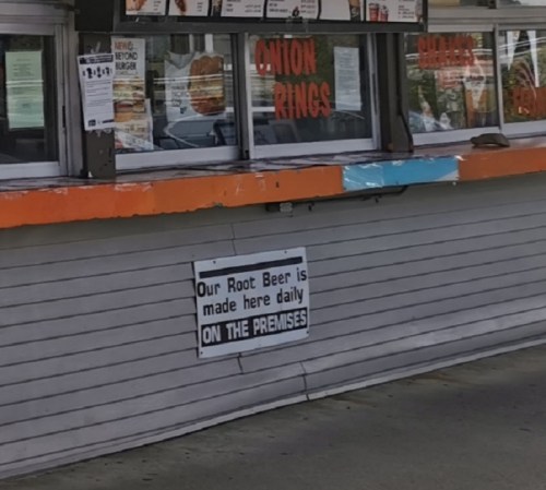 A fast-food stand with a menu display and a sign stating, "Our Root Beer is made here daily on the premises."