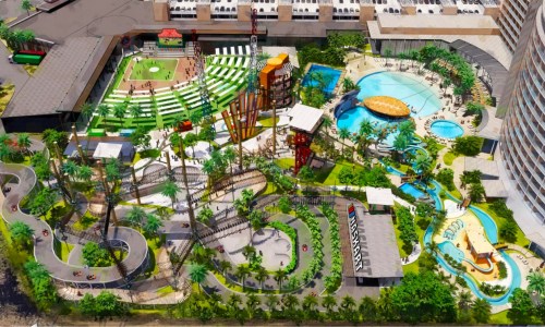 Aerial view of a vibrant amusement park featuring pools, slides, a sports field, and lush greenery.