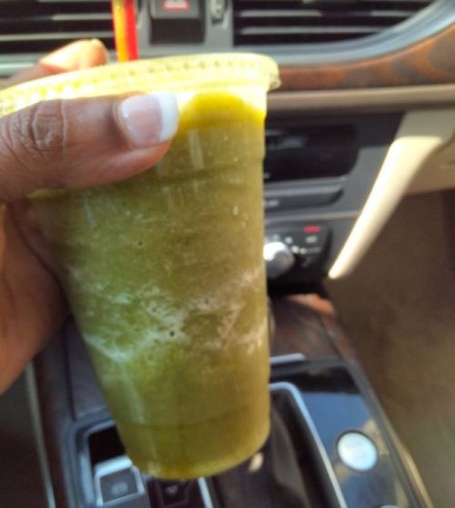 A hand holding a green smoothie in a cup, with a car interior visible in the background.