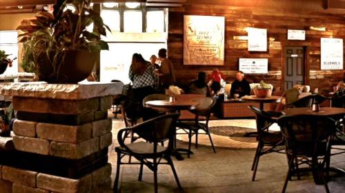 A cozy café interior with wooden walls, plants, and people chatting at tables.
