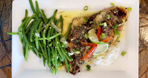 Grilled fish fillet with lime, served with rice and green beans, garnished with scallions and red pepper.