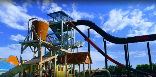 A tall water slide structure with a large funnel and two slides, set against a blue sky with clouds.