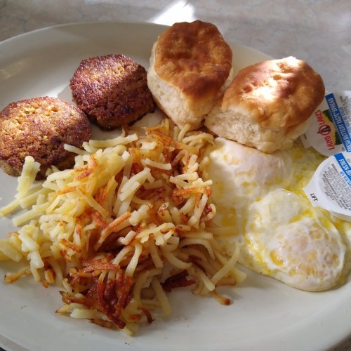 A plate of breakfast featuring two fried eggs, hash browns, two biscuits, and two sausage patties.