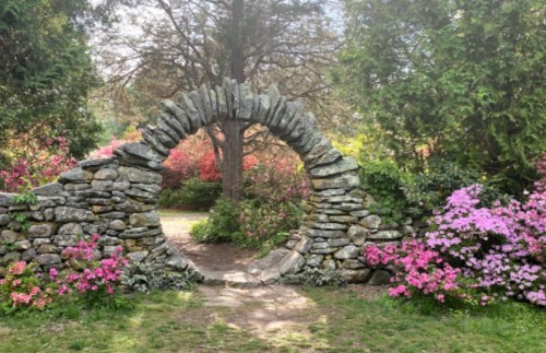 A stone archway surrounded by vibrant flowers and greenery, leading into a serene garden path.