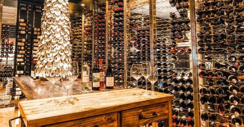 A stylish wine cellar featuring wooden shelves filled with bottles, a wooden table, and glasses ready for tasting.