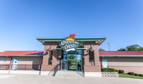 Exterior view of Adventure Oasis building with a colorful sign, clear blue sky, and landscaped entrance.