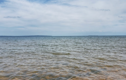 A calm sea under a cloudy sky, with gentle waves and distant land on the horizon.