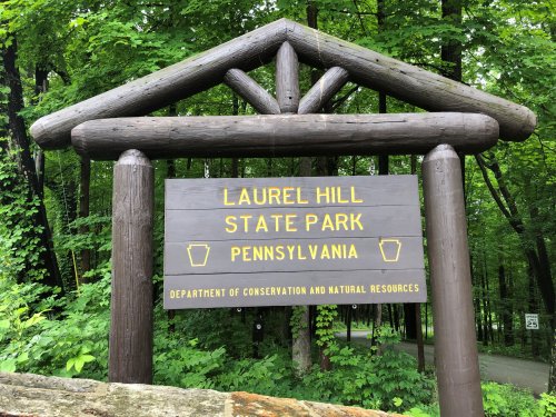 Sign for Laurel Hill State Park in Pennsylvania, featuring wooden beams and surrounded by lush greenery.