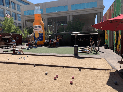 Outdoor scene with people playing games, a large Corona Extra bottle, and colorful murals in a lively setting.