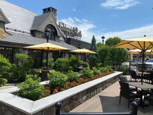 A charming restaurant exterior with outdoor seating, umbrellas, and lush greenery on a sunny day.