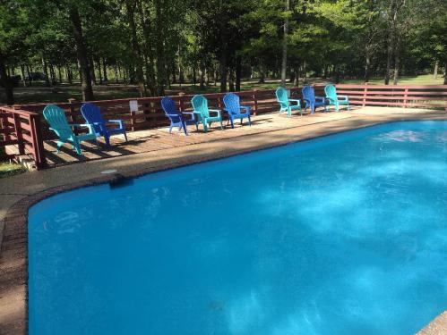 A clear blue swimming pool surrounded by green trees and blue chairs on a wooden deck.