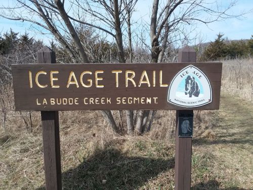 Sign for the Ice Age Trail, La Budde Creek Segment, surrounded by grassy terrain and trees.