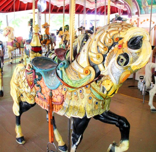 A colorful, ornate carousel horse with intricate designs, set against a backdrop of other carousel animals.