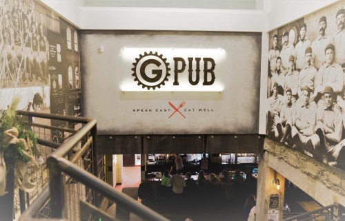 Interior view of G PUB, featuring a logo and vintage photos on the walls, with a staircase leading to the dining area.