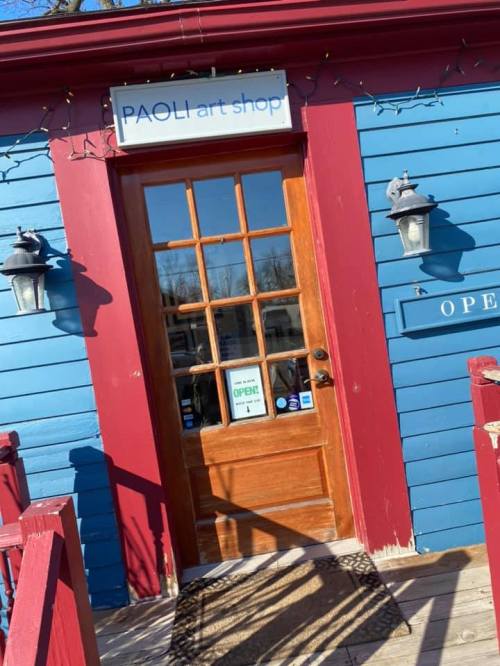 A blue and red building with a wooden door labeled "PAOLI art shop" and an "OPEN" sign in the window.