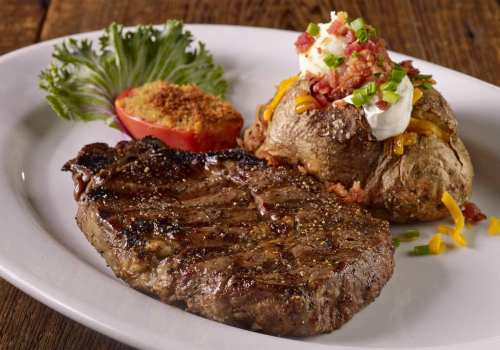 A grilled steak served with a baked potato topped with cheese, bacon, and sour cream, alongside a slice of tomato and lettuce.