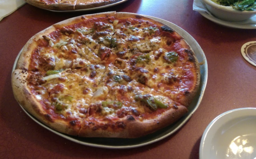 A freshly baked pizza topped with cheese, green peppers, and meat, served on a round metal tray.