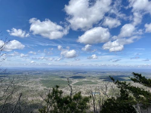 A panoramic view of rolling hills and valleys under a blue sky filled with fluffy white clouds.