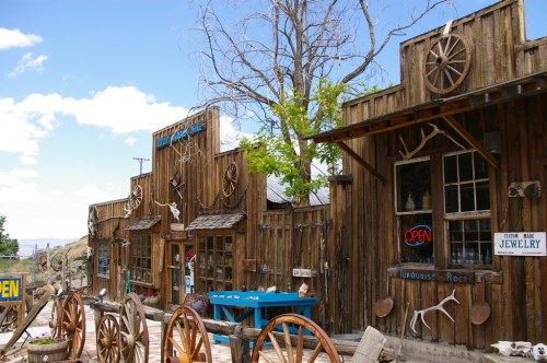 A rustic wooden storefront with wagon wheels, an "Open" sign, and a clear blue sky in the background.