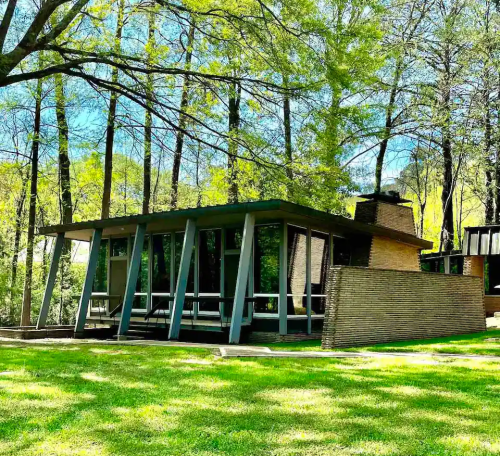 A modern house with large windows, set among trees and grass, featuring a unique architectural design.