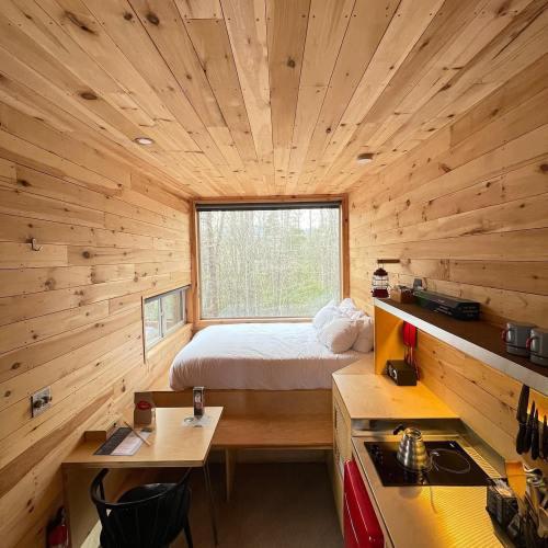 Cozy wooden interior of a small cabin featuring a bed, kitchenette, and large window with a view of nature.