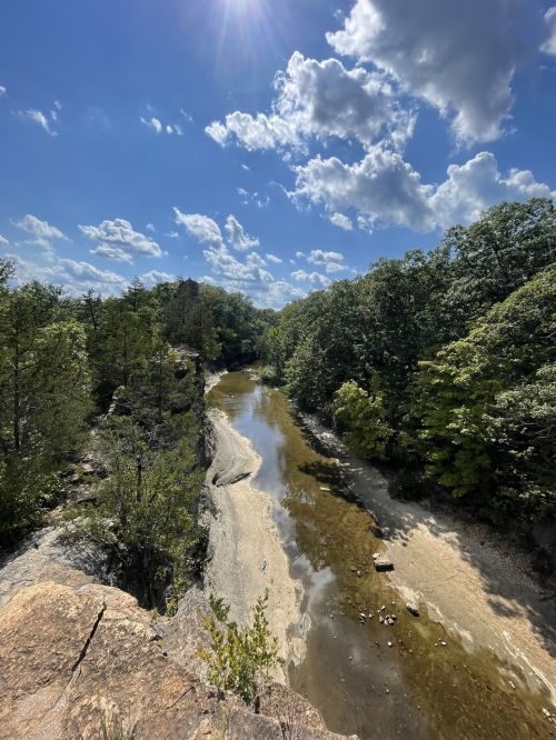 A scenic view of a river winding through lush greenery under a bright blue sky with fluffy clouds.