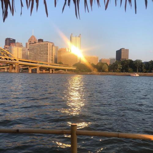 City skyline reflecting on water at sunset, with a bridge in the foreground and buildings in the background.