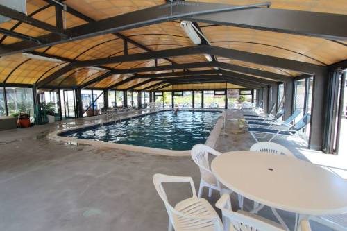 Indoor swimming pool area with a clear roof, surrounded by lounge chairs and tables. Bright and spacious atmosphere.