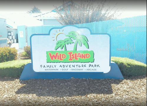 Sign for Wild Island Family Adventure Park featuring palm trees and activities like waterpark, golf, raceway, and arcade.