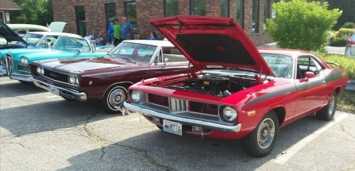 Two classic cars parked side by side, one red and one dark brown, with hoods open showcasing their engines.