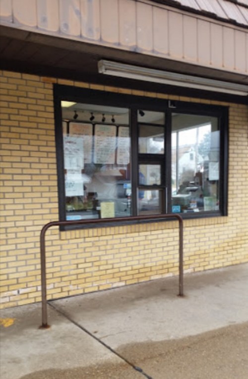 A brick building with a window displaying menus and signs, featuring a metal railing in front.