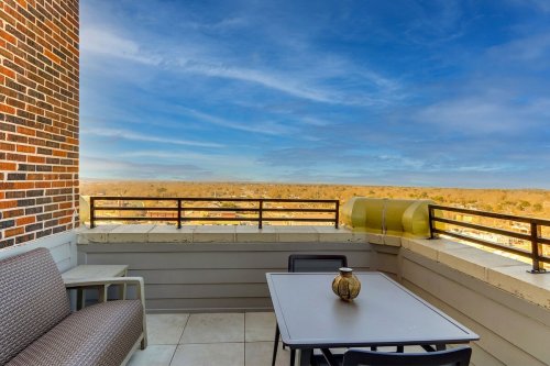 A balcony with a table and chairs, overlooking a scenic view of trees and a blue sky.
