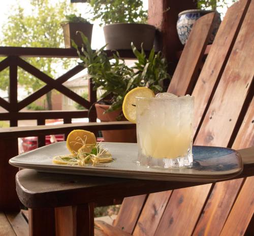 A refreshing cocktail with lemon slices sits on a tray beside a wooden chair, surrounded by greenery.