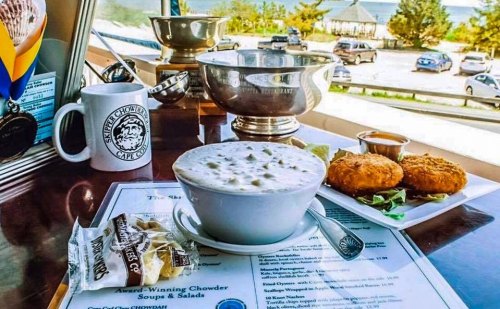 A bowl of clam chowder with crab cakes, a menu, and a trophy in a cafe with a view of the ocean.
