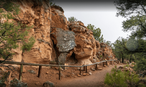 A winding dirt path alongside rocky cliffs and greenery in a natural landscape.