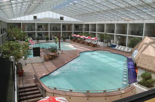 Indoor pool area with a glass roof, featuring lounge chairs, umbrellas, and a water slide.